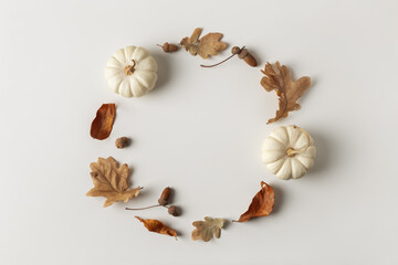 Minimalist autumnal composition with decorative white pumpkins, withered leaves and acorns. Natural frame with copy space for your text or individual brand..