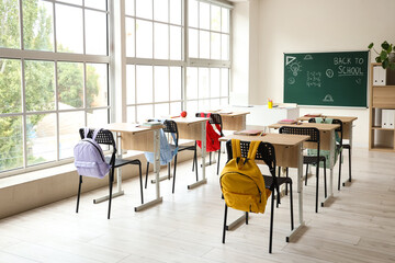 Interior of empty classroom with school desks and text BACK TO SCHOOL on chalkboard