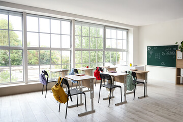 Interior of empty classroom with school desks and text BACK TO SCHOOL on chalkboard