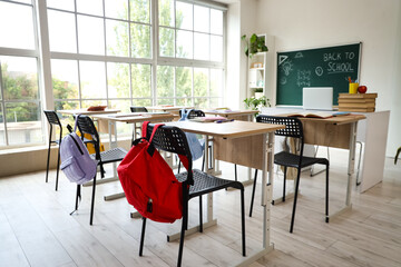 Interior of empty classroom with school desks and text BACK TO SCHOOL on chalkboard