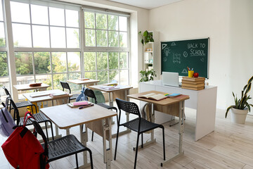 Interior of empty classroom with school desks and text BACK TO SCHOOL on chalkboard