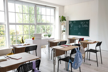 Interior of empty classroom with school desks and text BACK TO SCHOOL on chalkboard