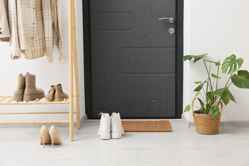 Rack with clothes, shoes and houseplant near door mat in hall
