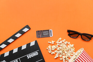 Movie clapper with cinema ticket, glasses and popcorn on orange background