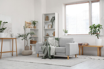 Cozy sofa with plaid, shelving units and houseplants in interior of living room