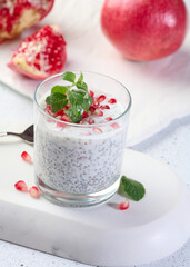 Glass with chia and yogurt dessert decorated with fresh fruits and pomegranate seeds on white table