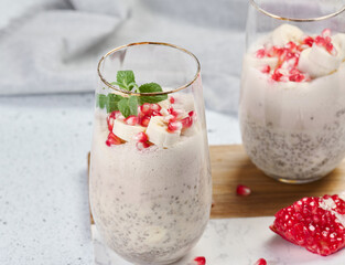 A glass of chia seeds and yogurt, with banana pieces and pomegranate seeds added to the dessert