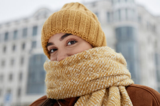 Close up portrait of cute girl wearing knit hat in winter and wrapped in scarf looking at camera with big hazel eyes copy space