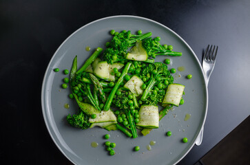 Warm green spring salad with asparagus, broccoli, peas, zucchini and olive oil, vegan healthy lunch salad in a grey plate
