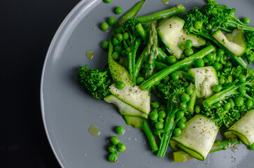 Warm green spring salad with asparagus, broccoli, peas, zucchini and olive oil, vegan healthy lunch salad in a grey plate