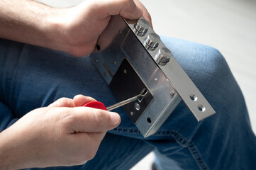 The locksmith using a screwdriver to adjust a metal door lock mechanism, demonstrating a close-up...