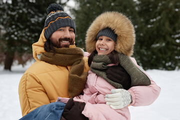 Waist up portrait of happy father holding daughter while playing together outdoors in winter and smiling at camera joyfully