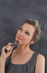 Obraz premium Chalkboard, mockup and thinking with teacher woman in classroom for development, education or lesson. Blackboard, idea and space with happy mature person at school for growth, learning or teaching