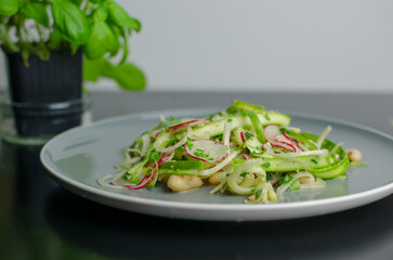 Fresh spring salad with asparagus ribbons, white beans and radish in the grey plate on the black table