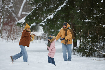 Candid full length shot of happy young family throwing snow at each other and having fun together in winter forest
