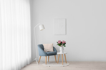 Armchair, lamp and coffee table with protea flowers in vase near white wall