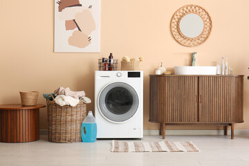 Modern washing machine, basket with laundry, chest of drawers and coffee table in room