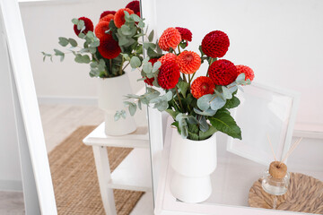 Dahlia flowers in vase on coffee table near mirror in room