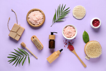 Composition with natural body scrubs, essential oil, bath supplies and palm leaves on lilac background