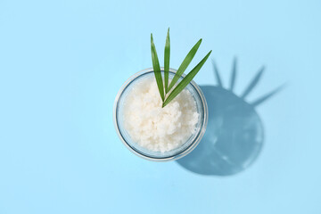 Glass jar with natural body scrub and palm leaf on color background