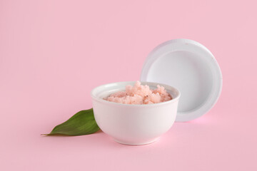 Bowl of natural body scrub and lid on pink background
