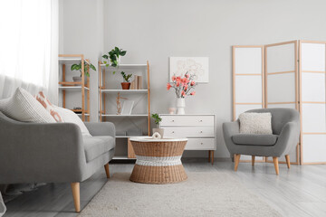 Interior of living room with sofa, armchair and magnolia flowers on chest of drawers