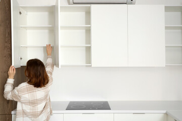 Young woman opening cupboard in kitchen, back view