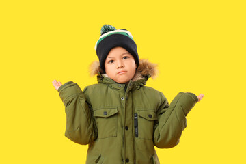 Cute little Asian boy in warm clothes on yellow background