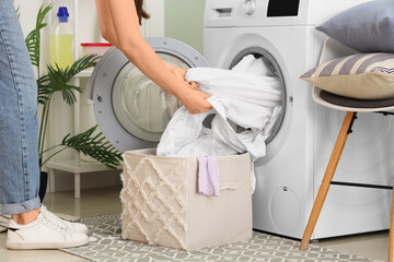 Woman taking white clothes from washing machine in laundry room