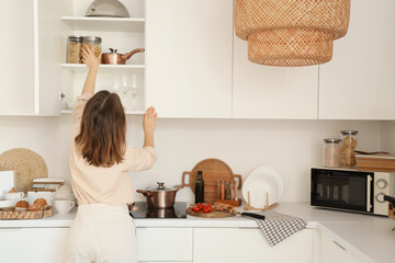Young woman taking jar of pasta from shelf in kitchen, back view