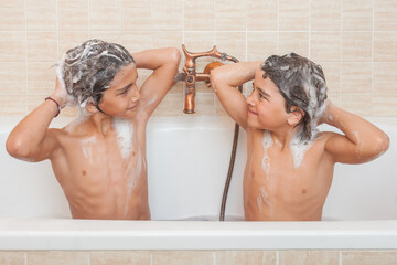 Two young boys are in a bathtub, one of them is washing his hair © OR MIXphoto