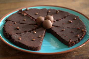 Fresh chocolate cake with chocolate sprinkles and pralines on top, on a blue plate