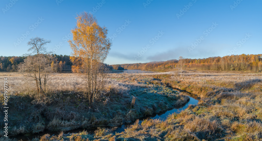 Aufkleber A autumn field with a river running through it and a tree in the foreground. The sky is blue and the sun is shining