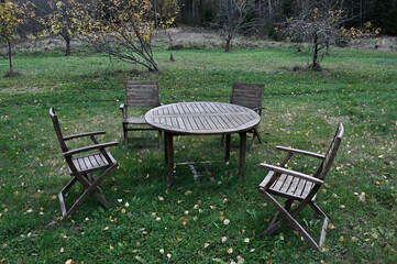 a rustic outdoor seating arrangement with a round wooden table and four wooden chairs set on green grass