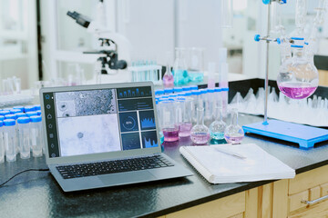 Laboratory scene featuring a laptop analyzing scientific data among various equipment and glassware, with a microscope in the background visible