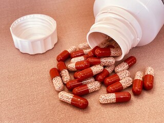 Red and transparent medication capsules pouring from bottle containing pancreatic enzyme