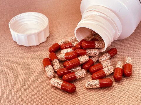 Red and transparent medication capsules pouring from bottle containing pancreatic enzyme
