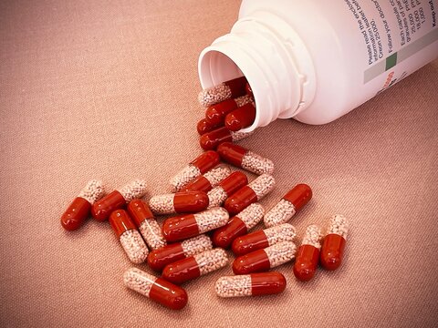 Red and transparent medication capsules pouring from bottle containing pancreatic enzyme