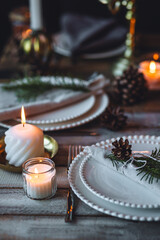 Rustic elegant table decor for christmas family dinner. Center piece with white candle, pine cone, fir tree branches. Zero waste eco-friendly home decoration. Cozy atmosphere, wooden background.