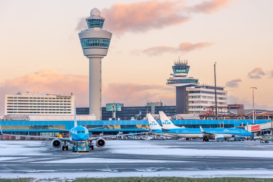 Winter images of Schiphol Airport Amsterdam with blue KLM Royal Dutch Airlines airplanes in snow and ice with orange sunrise morning