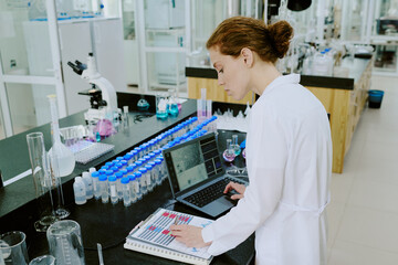 Female scientist working with lab equipment and analyzing data on a laptop surrounded by scientific...
