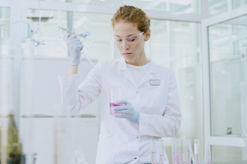 Scientist in laboratory coat and safety glasses conducting experiment with liquid in test tube....