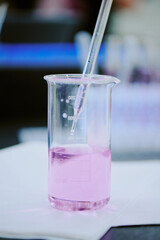 Laboratory scene with a beaker filled with purple liquid while a pipette is being inserted for measurement purposes. The focus is on the precise measurement process