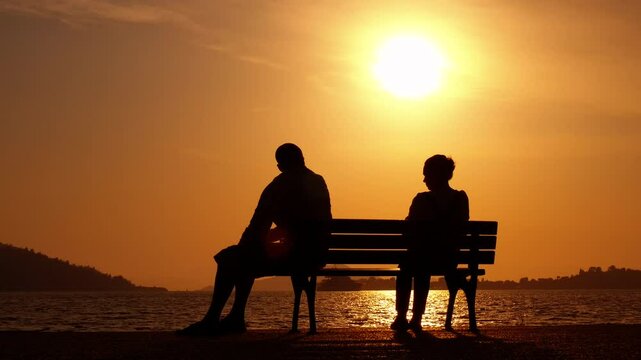 Quarrel on the bench. A view of stressed couple silhouette sitting separately on the bench during nightfall time.