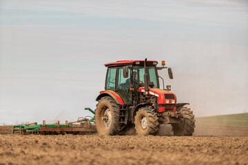 Farmer works the land, plowing a field with a modern red tractor on a sunny day