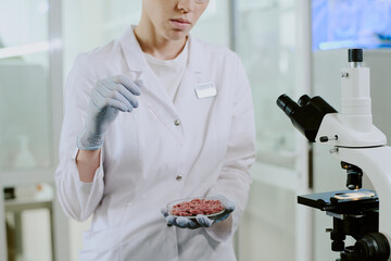 Researcher wearing lab coat and gloves examining lab-grown meat sample in modern laboratory setting...