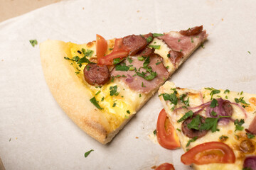 Pizza slices with sausage, ham, tomato, red onion, and parsley in a box on parchment paper. One slice has a bite out. Perfect for casual dining and pizza lover themes.