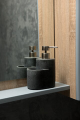 Close-up of a dark stone-textured soap dispenser and toothbrush holder on a light shelf in a bathroom. The metallic pump adds a modern touch. Perfect for contemporary and minimalist themes.