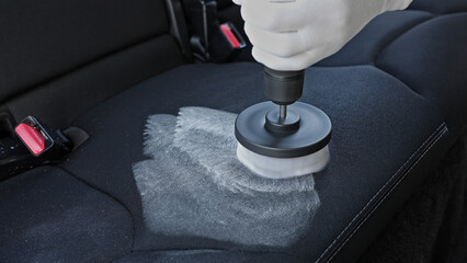 Professional car cleaning. Worker uses professional brush tool to clean car seat upholstery leaving...