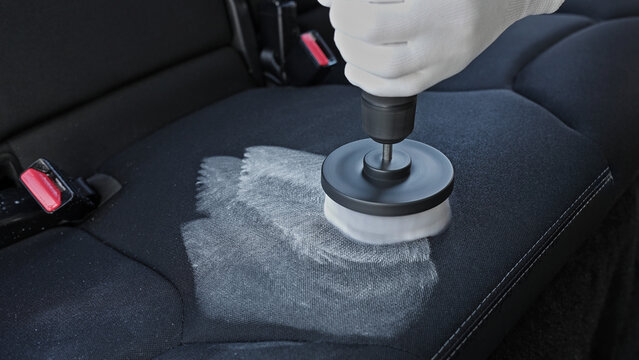 Professional car cleaning. Worker uses professional brush tool to clean car seat upholstery leaving a foam trail. Advertising concept for professional car cleaning. Copy space. Backdrop.